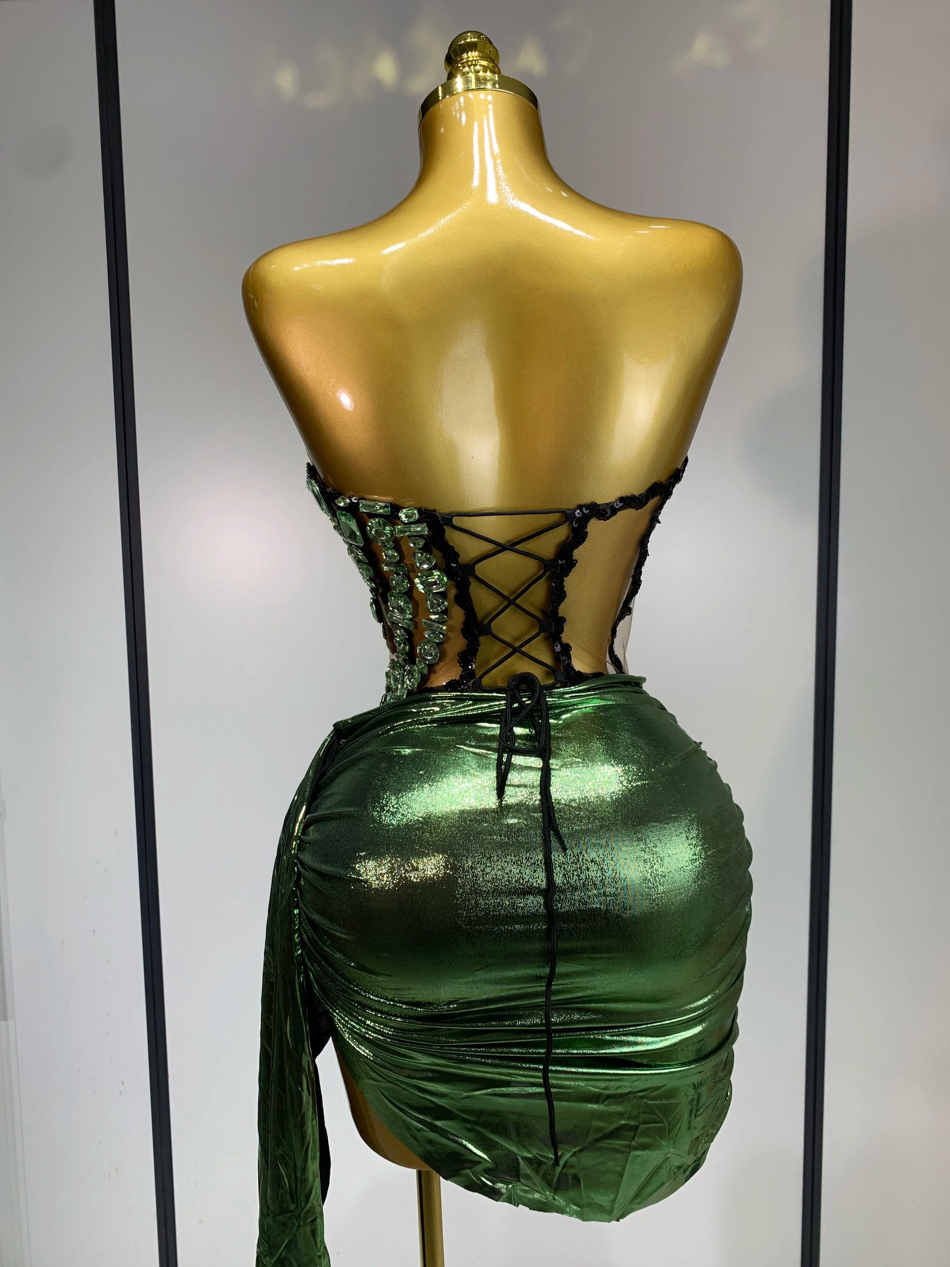 Mannequin wearing a green metallic dress with lace-up back against a neutral background