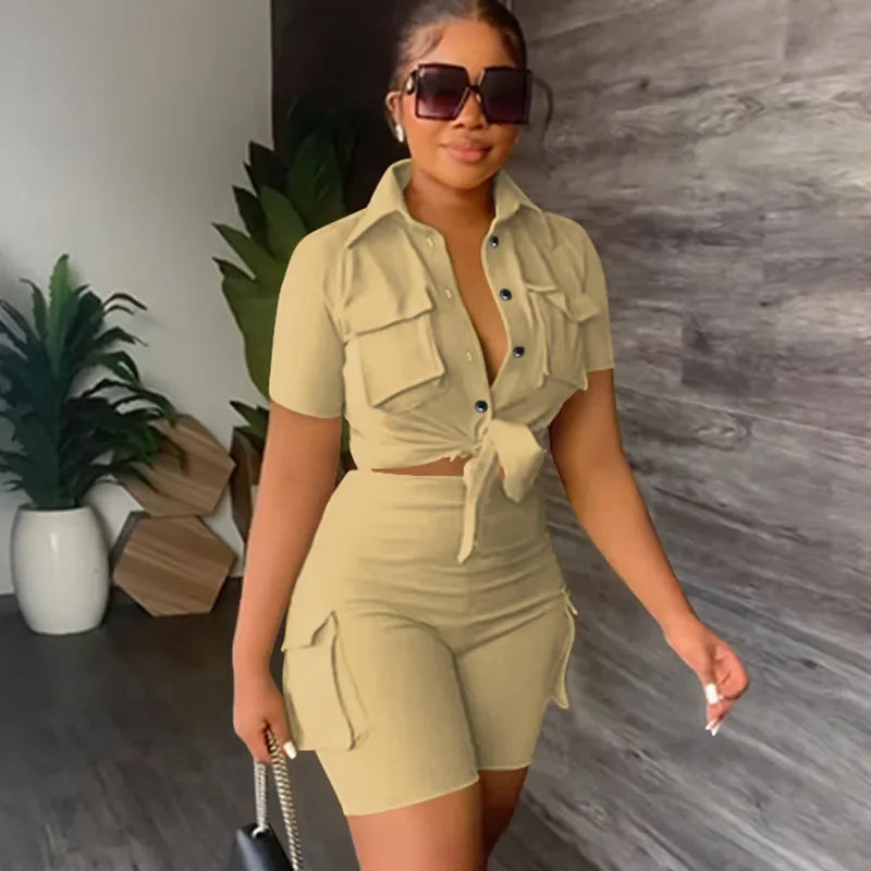 Woman in a beige outfit standing indoors with plants and a gray wall in the background