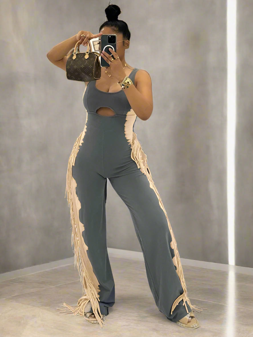 Woman taking a mirror selfie wearing a gray jumpsuit with fringe details in an indoor setting.