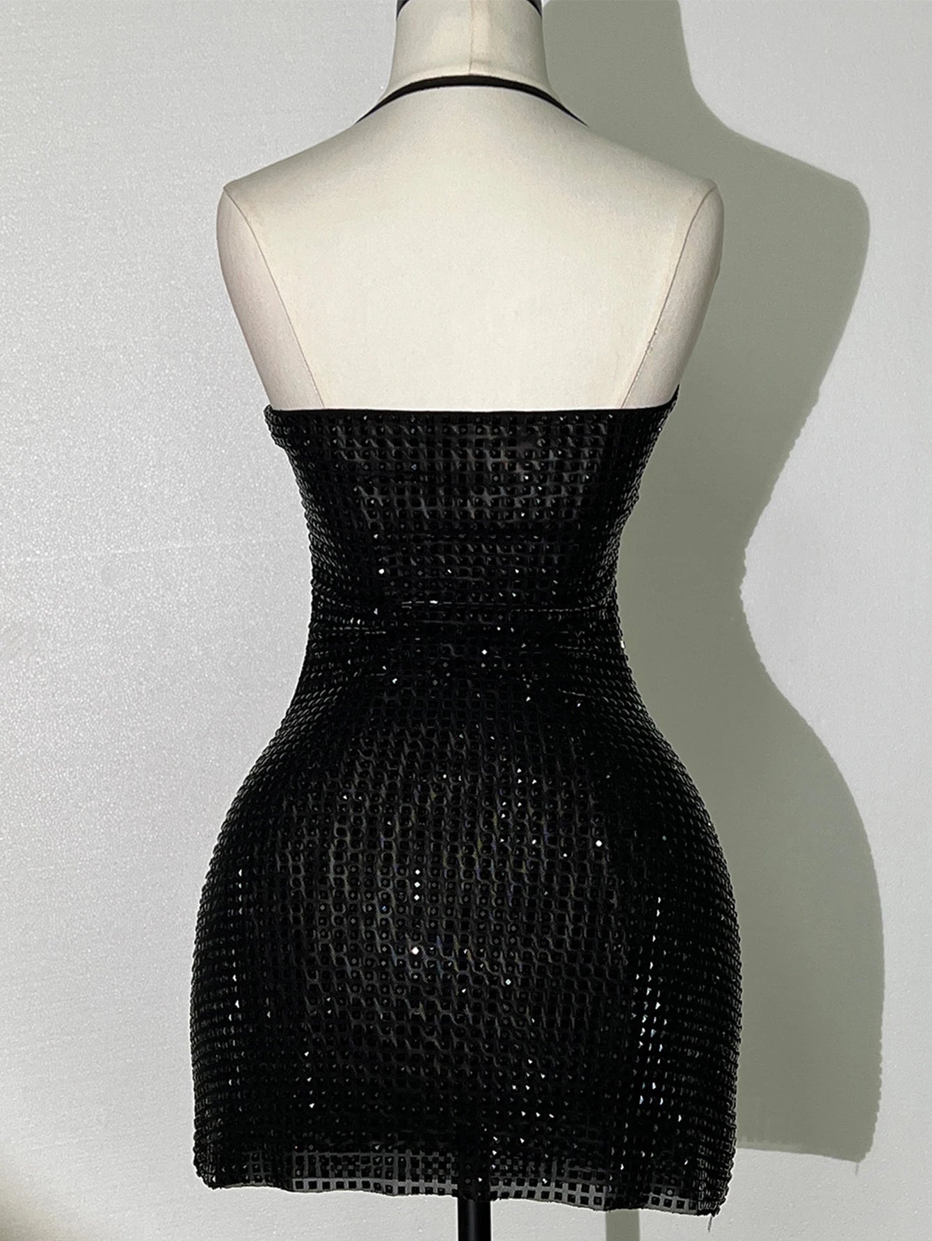 Black beaded dress on a mannequin against a plain background