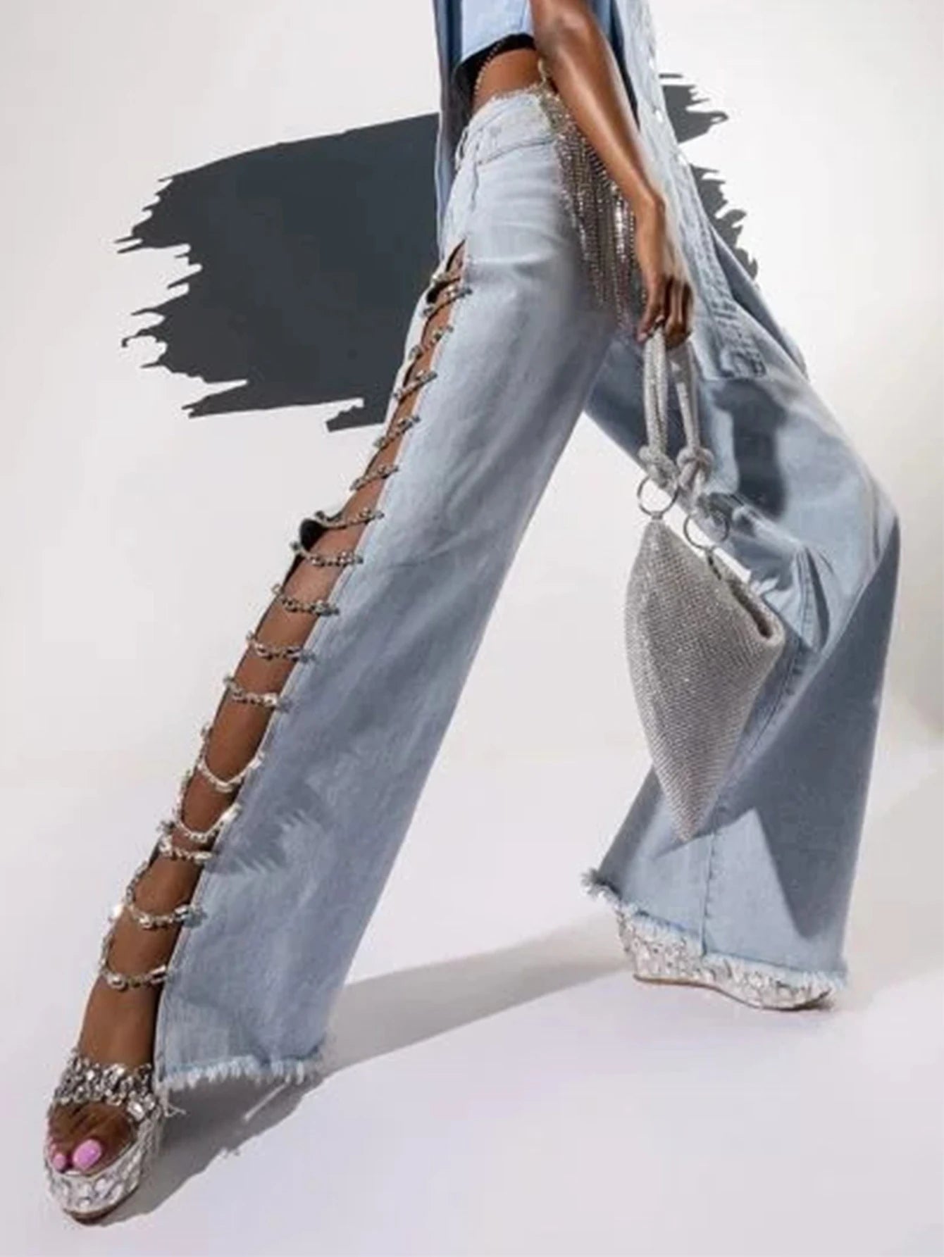Person wearing light blue jeans with embellishments, holding a sparkly handbag on a white background.