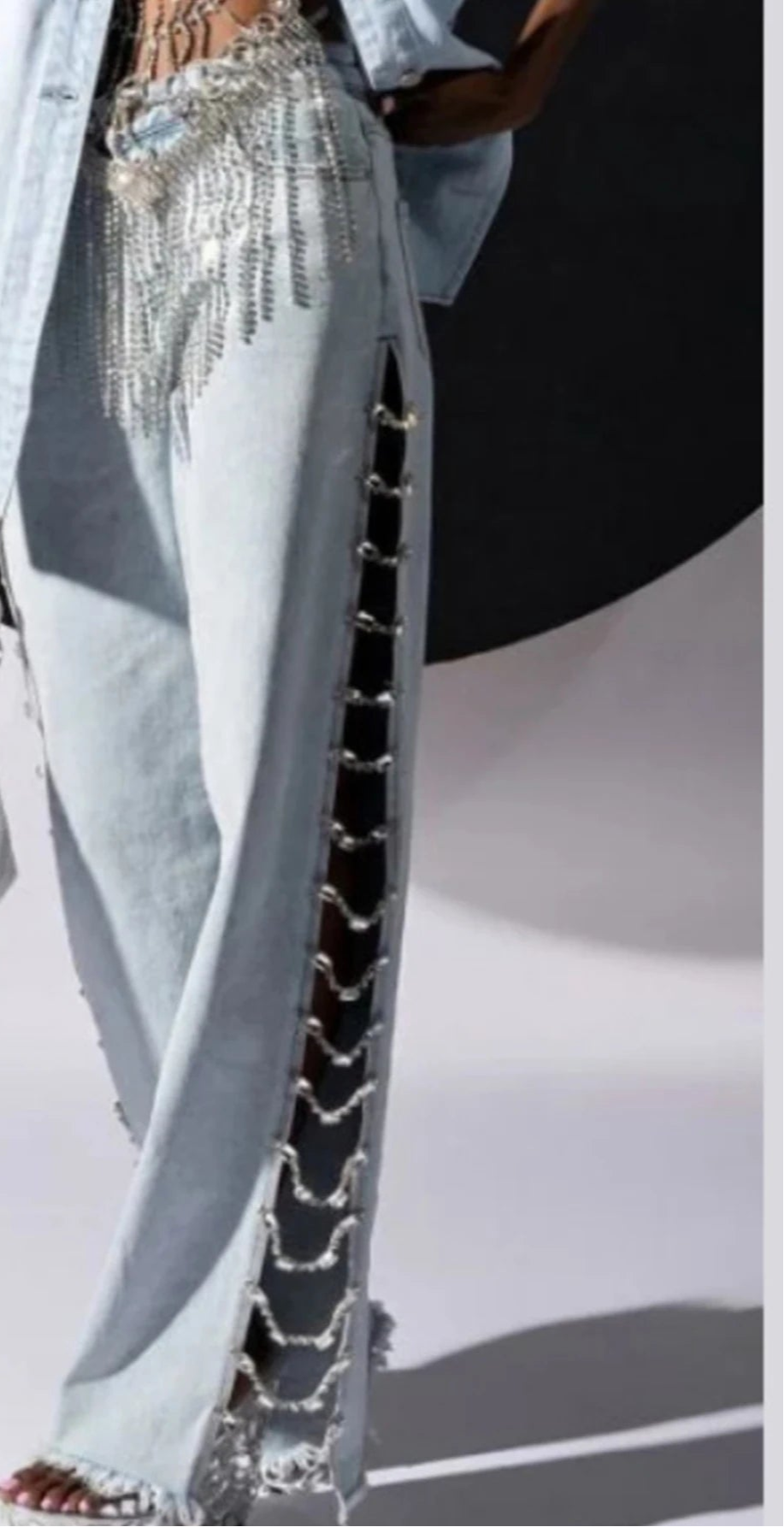 Close-up of a person wearing light blue pants with decorative chains and a white jacket.