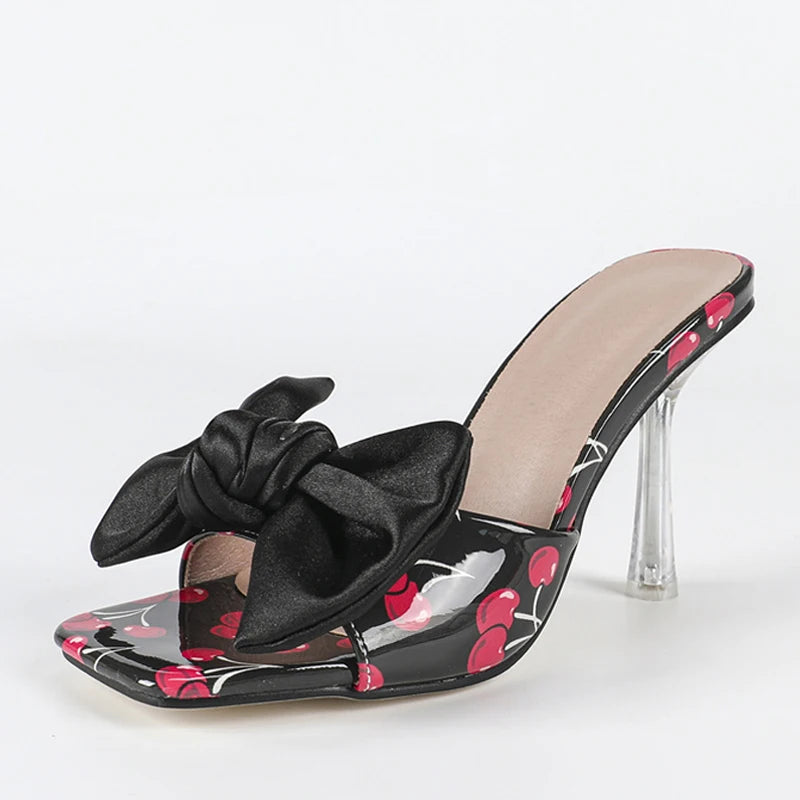 Black high-heeled shoe with a bow and red cherry design on a white background