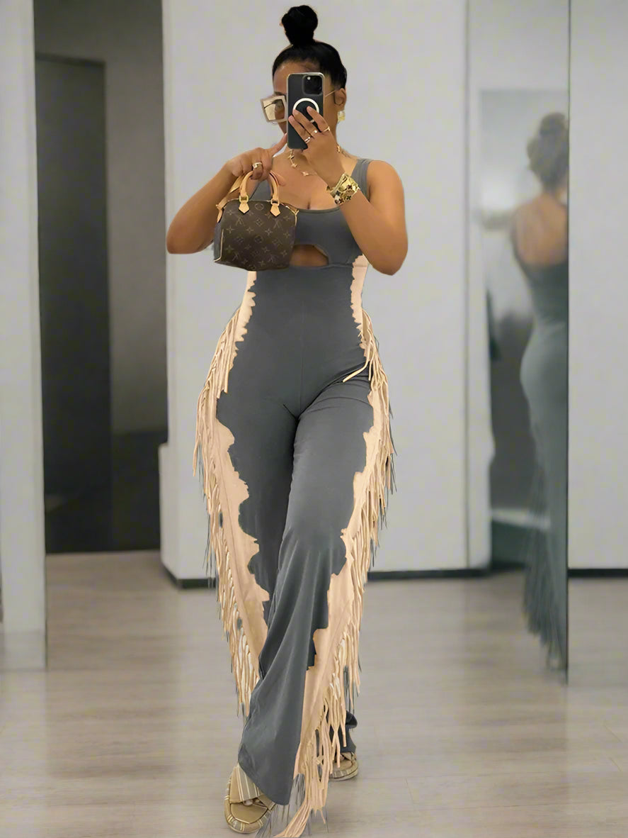 Woman in a gray outfit with tassels taking a mirror selfie in an indoor setting.