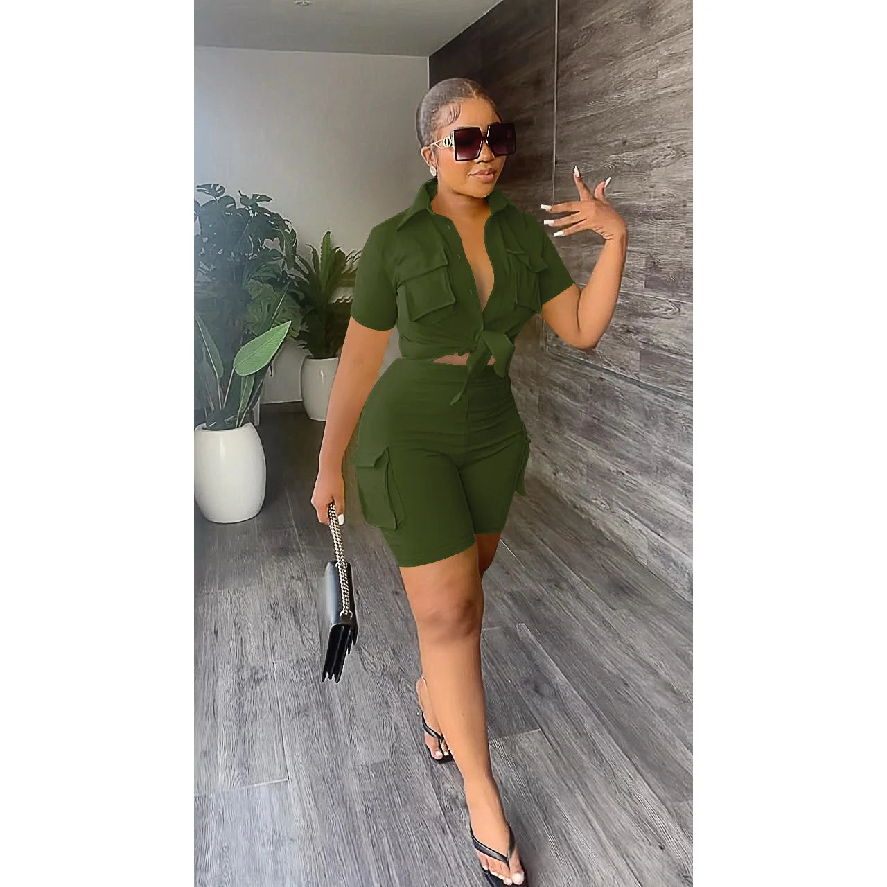 Woman in a green outfit posing in a room with plants and wooden flooring.