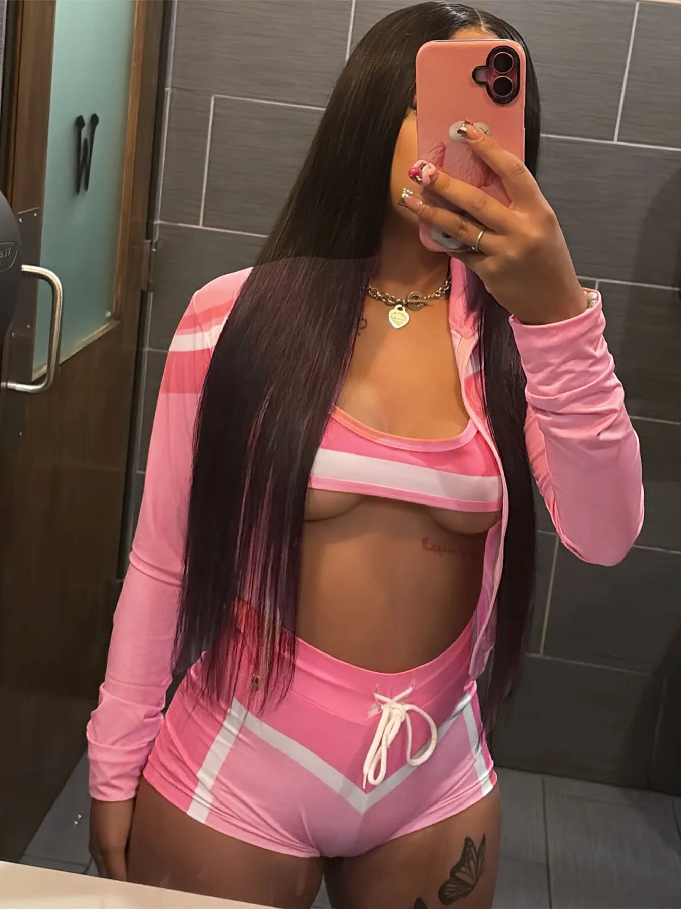 Person wearing a pink outfit taking a mirror selfie in a bathroom.