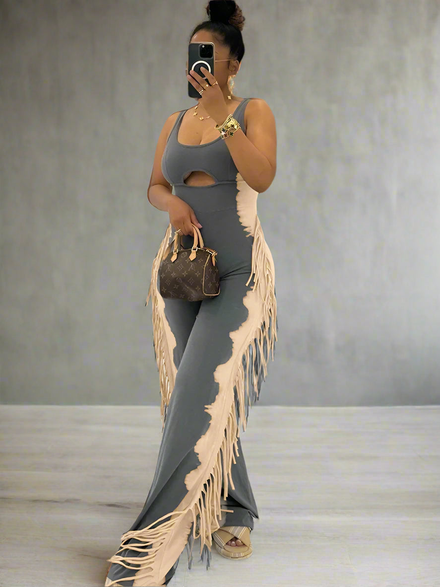 Woman in a gray jumpsuit with fringe holding a handbag indoors.