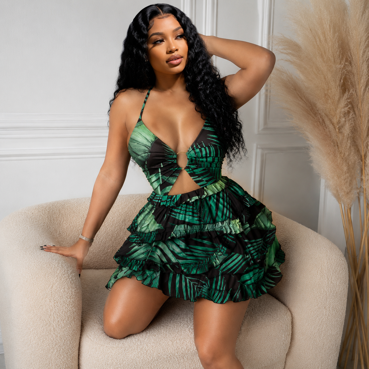 Woman in a green and black patterned dress sitting on a beige chair.